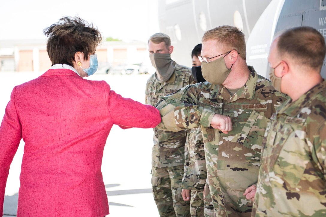 A civilian woman exchanges an elbow bump with one of several airmen she is meeting. All are wearing face masks.
