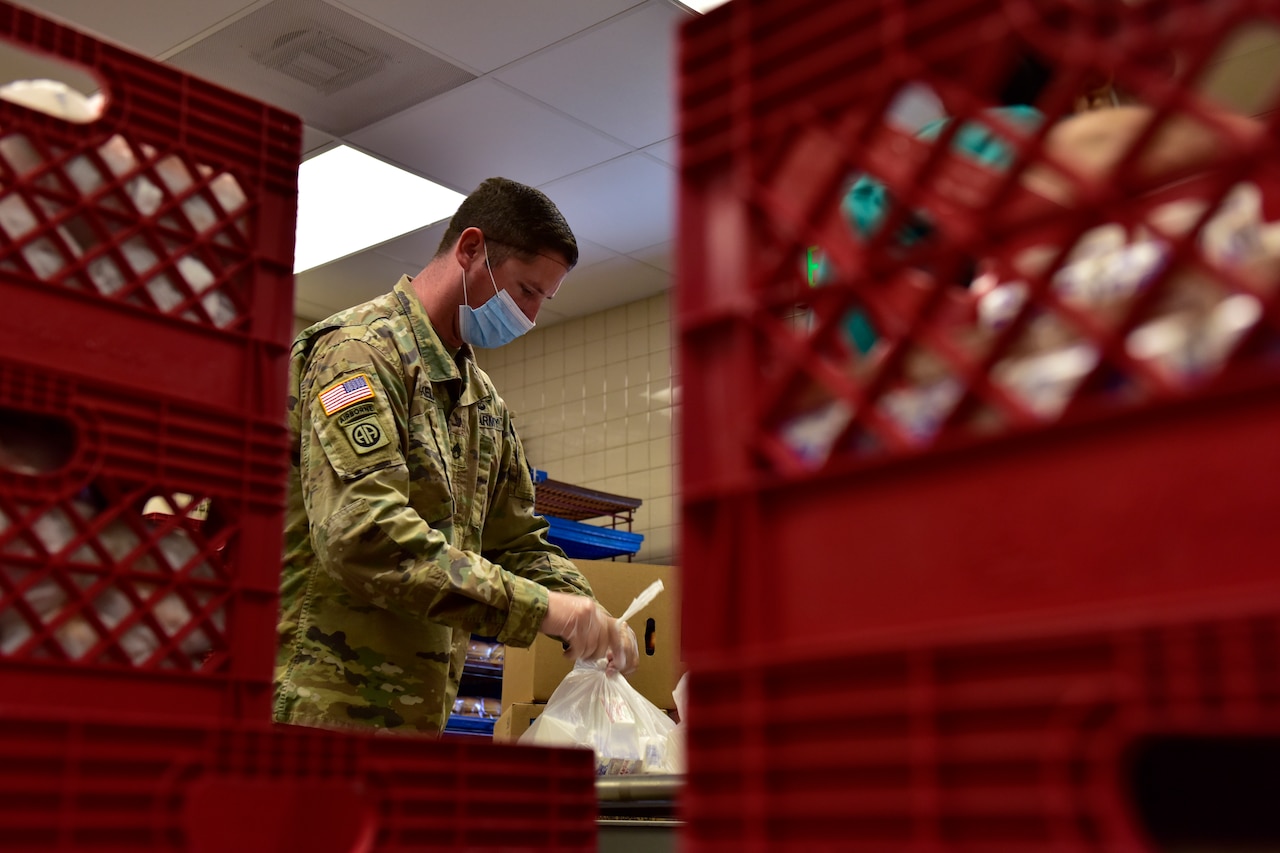 A soldier wearing a face mask packs a school lunch.