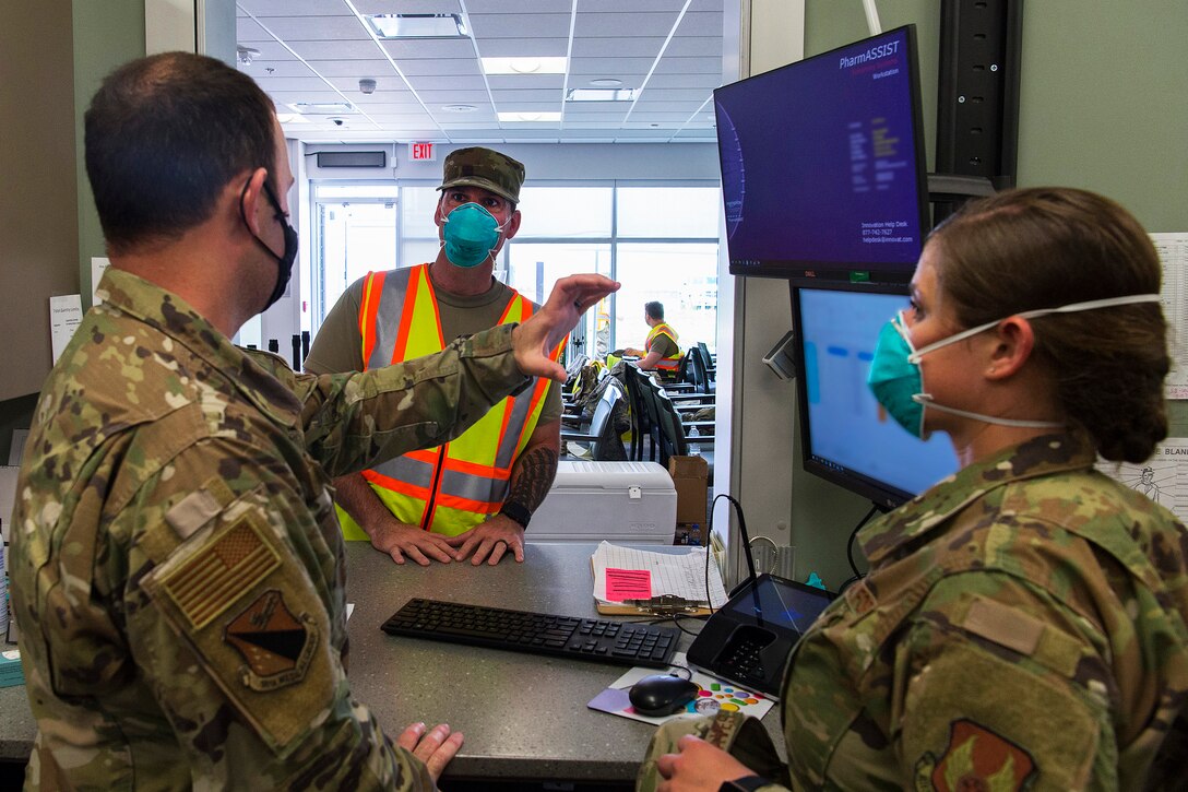 Three military personnel wearing face masks and gloves fill a customer’s prescriptions.