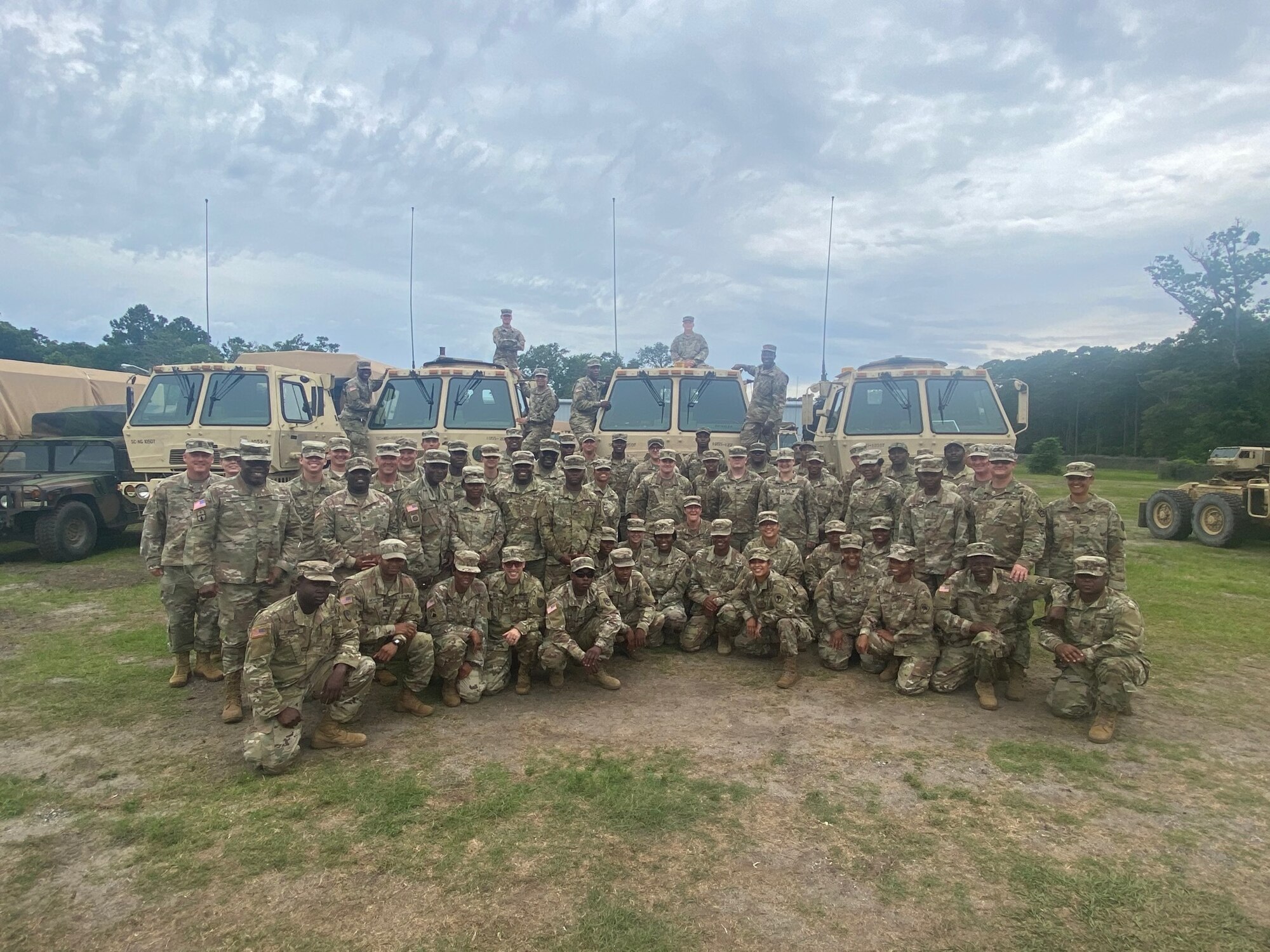 Soldiers pose in front of Army trucks