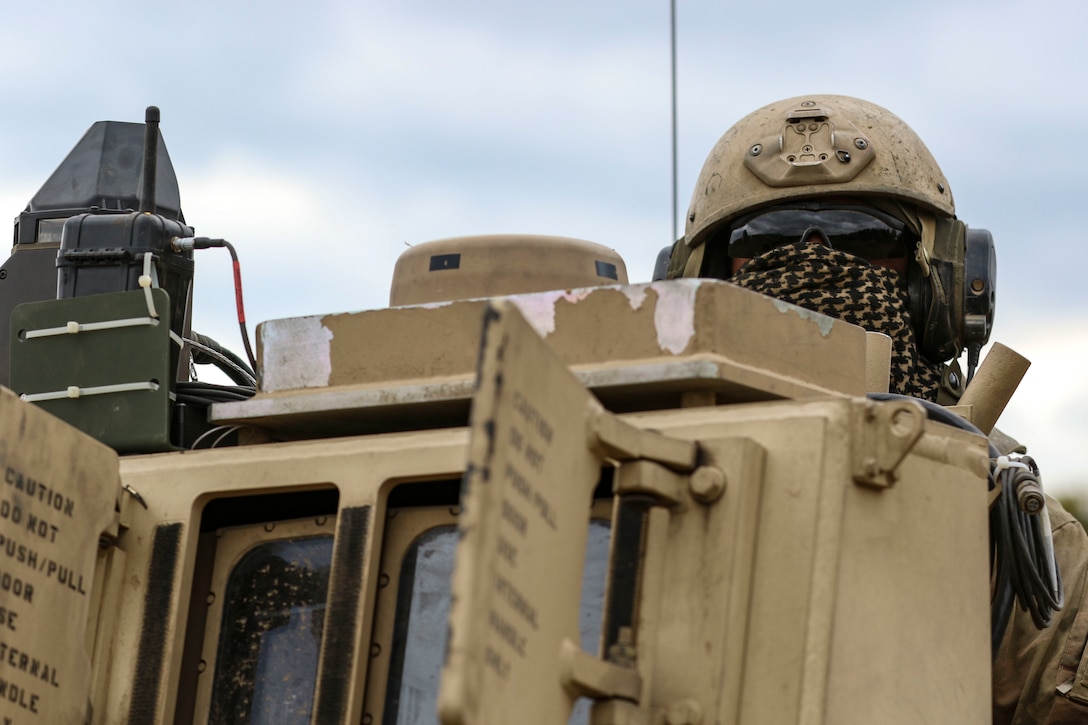 A soldier wearing a mask looks through dark glasses from a military vehicle.