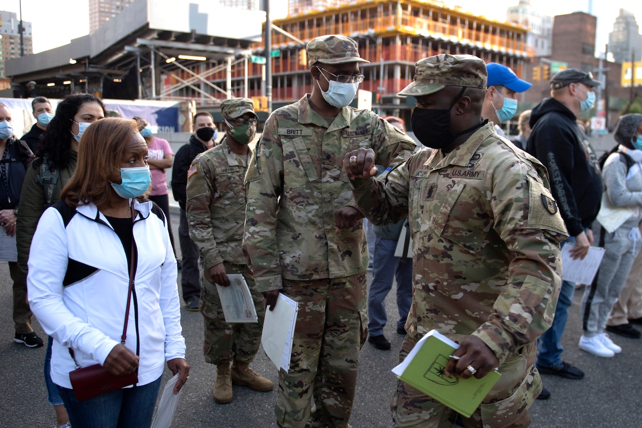 Soldiers wearing face masks stand outside in a large group of people.