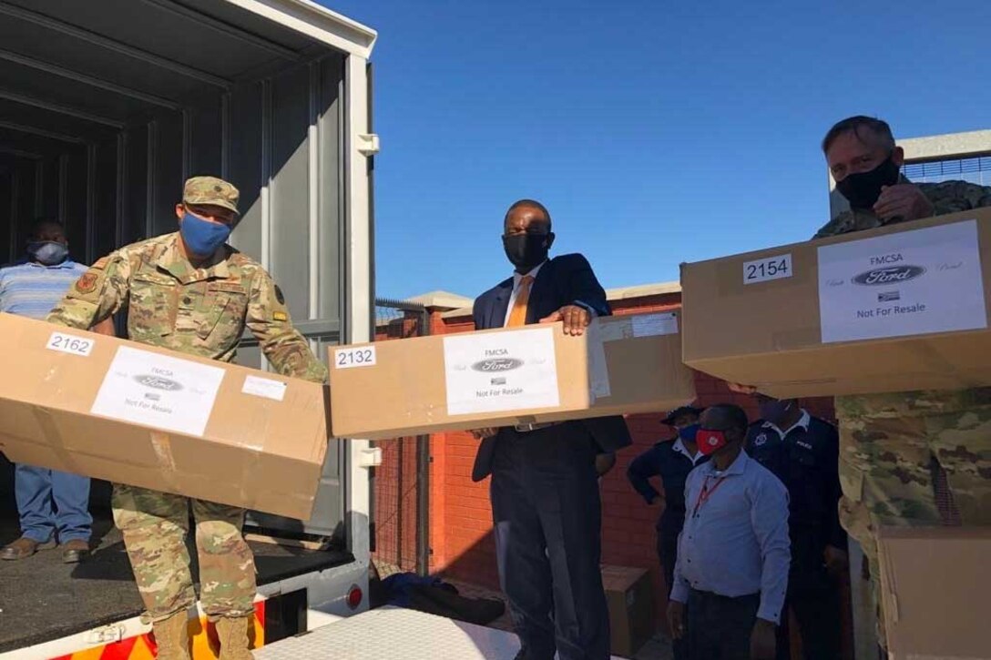 Two service members and a civilian carry cardboard boxes.