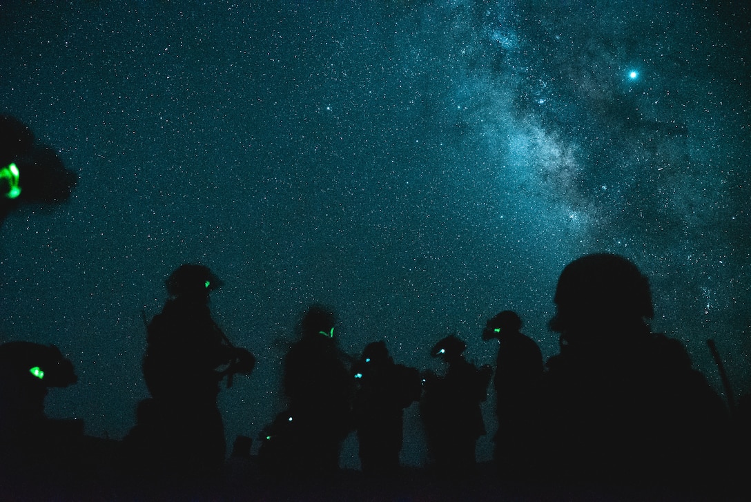 Multiple service members stand in silhouette before a star-illuminated night sky.