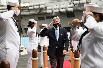 Secretary of the Navy Kenneth J. Braithwaite renders honors as he passes through sideboys upon arrival aboard the aircraft carrier
