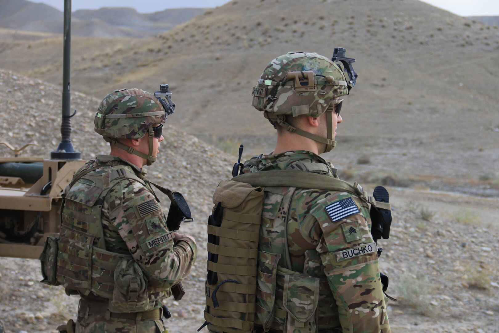 Two uniformed service members look out over desert terrain.