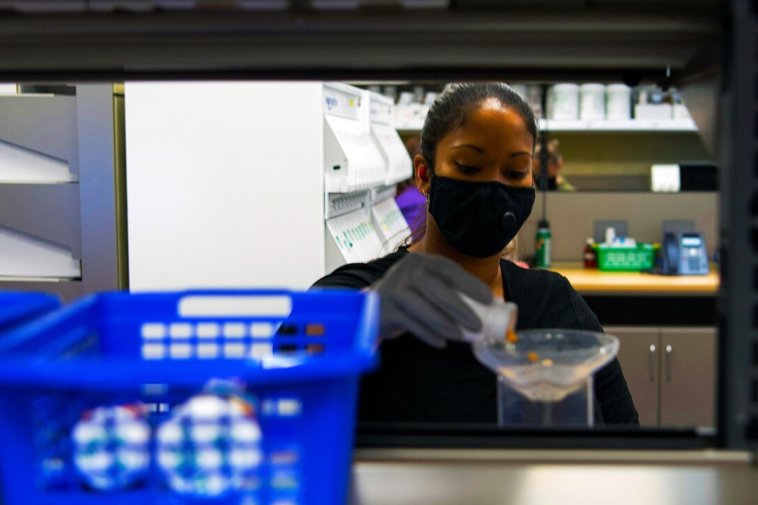 A soldier wears personal protective equipment while she fills a customer’s prescription at a military pharmacy.