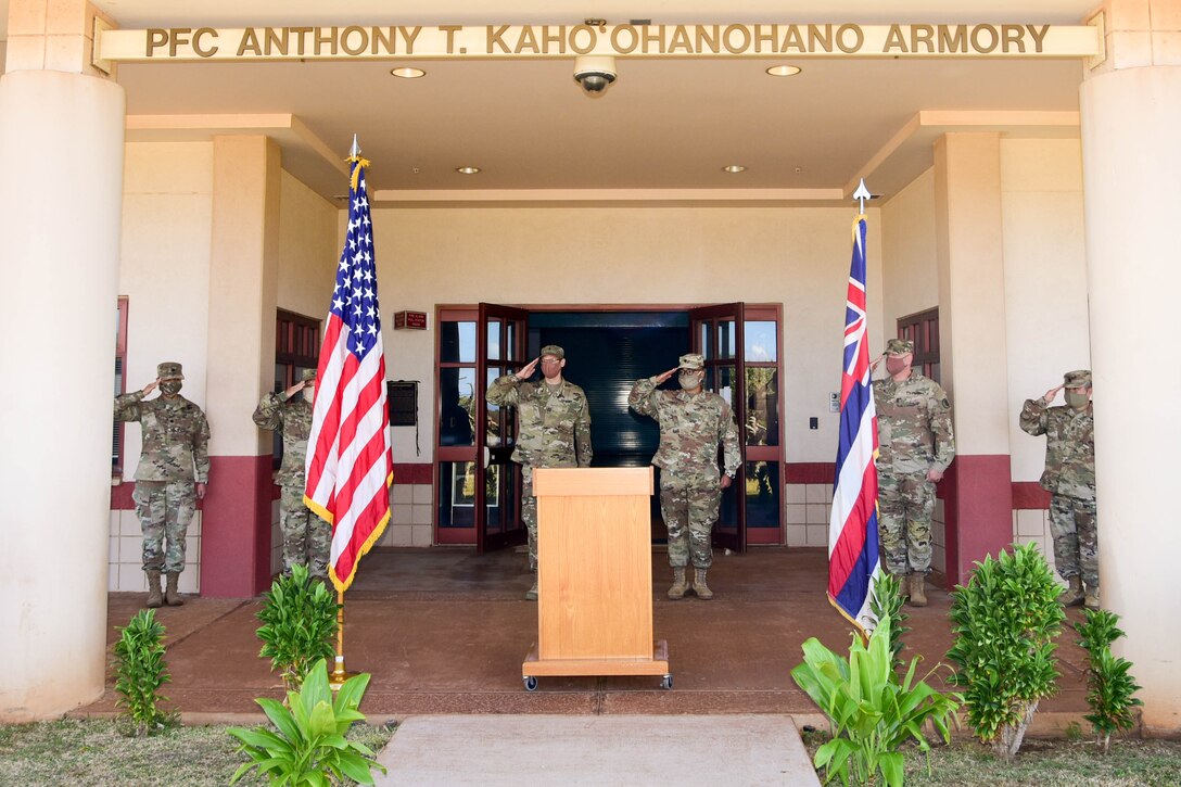 Six soldiers salute near a lectern at the entrance to a building.