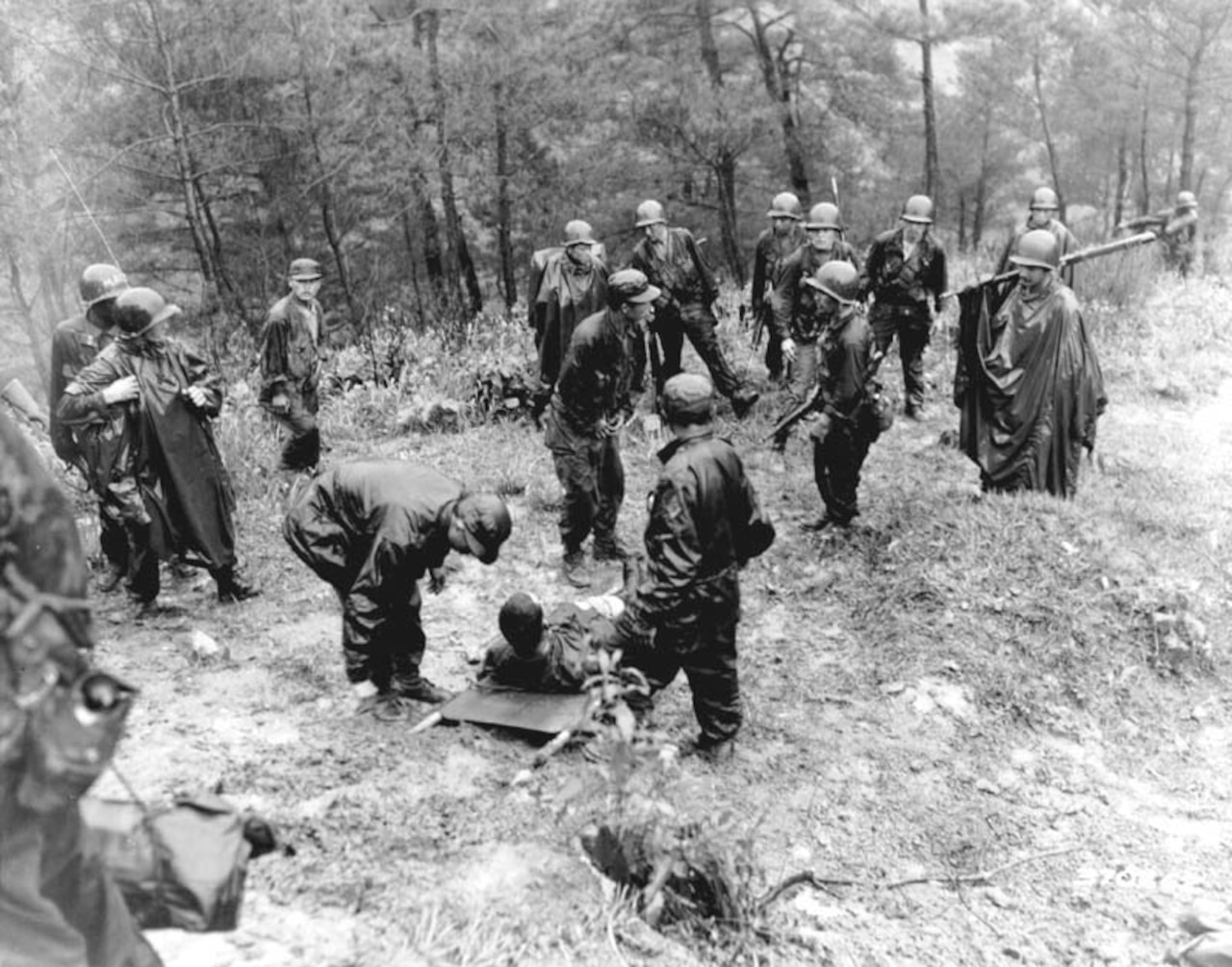 Several soldiers on a hill stand near a soldier on a stretcher.