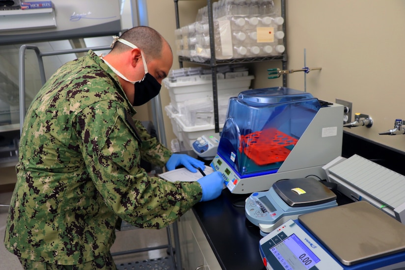 A soldier wearing personal protective equipment inspects laboratory equipment for COVID-19 testing.
