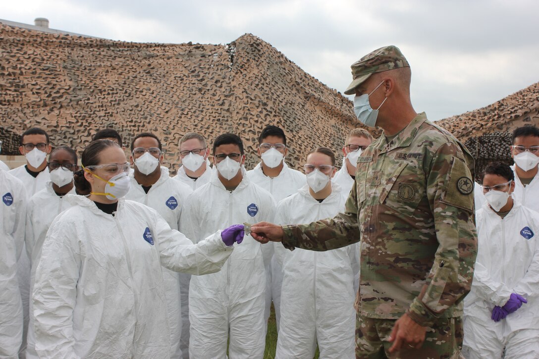 A military officer presents a coin to a soldier in a medical uniform as other  people stand behind her.