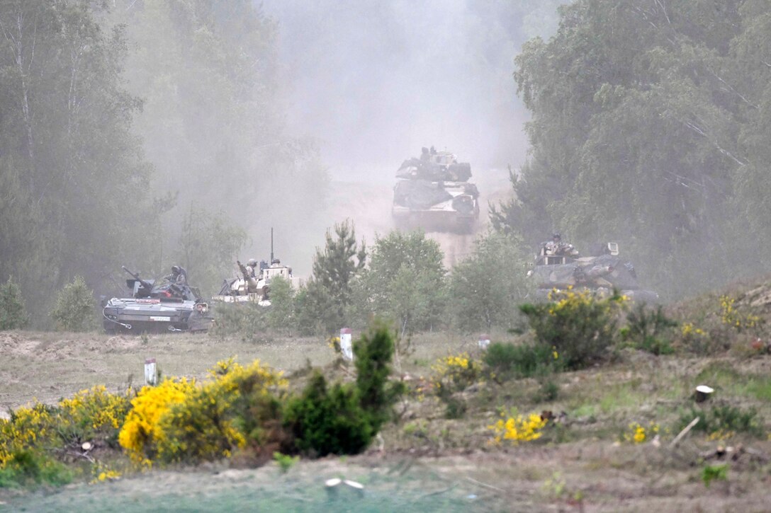 U.S. and Polish soldiers drive tanks in a forest-like area.