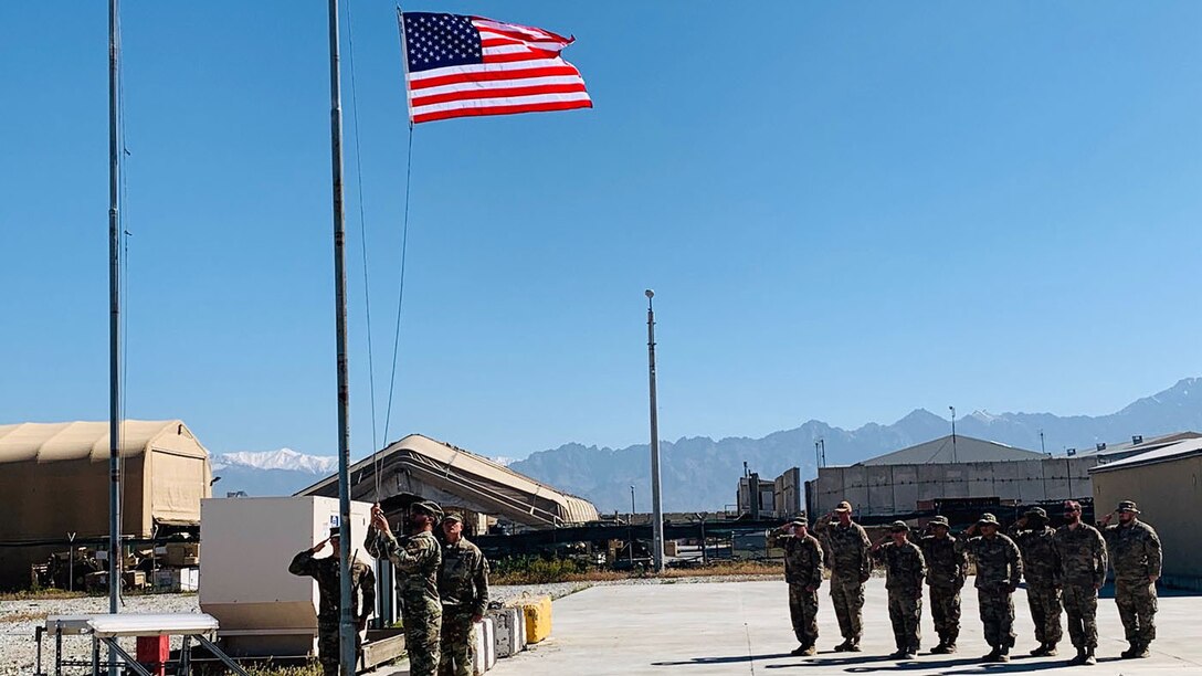 Service members raise and salute a flag going up a pole