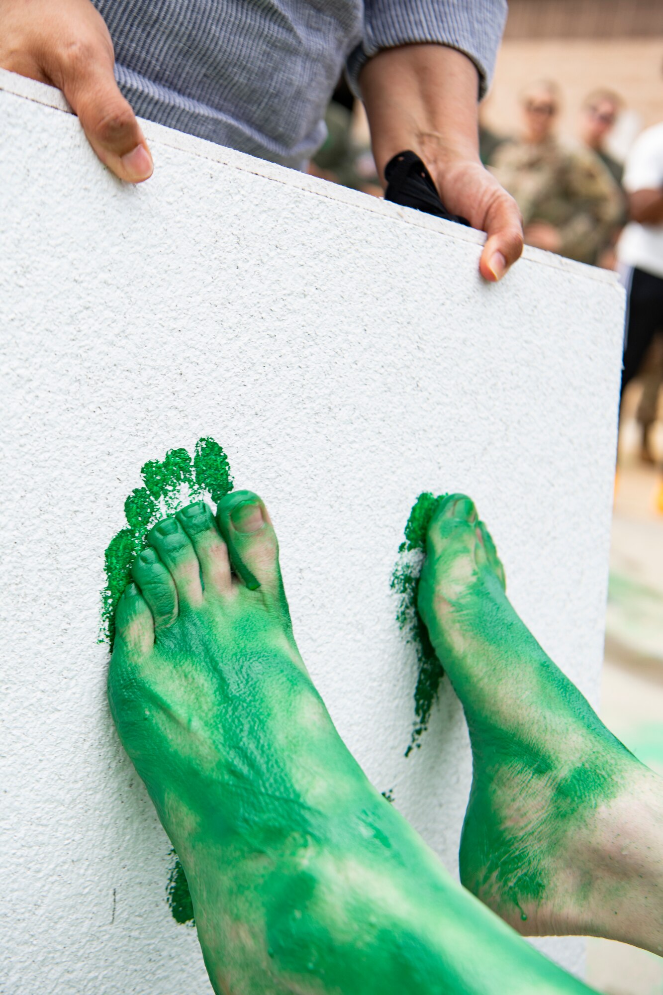 A photo of a an Airman pressing painted feet against a ceiling tile