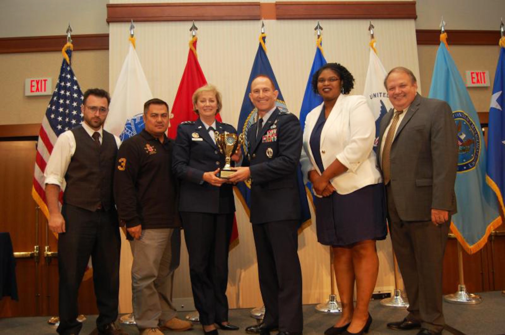 A group photo of military and civilian personnel smile while holding an award