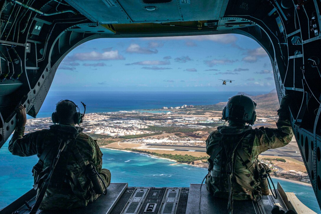 Two soldiers sit in the back of an open helicopter.