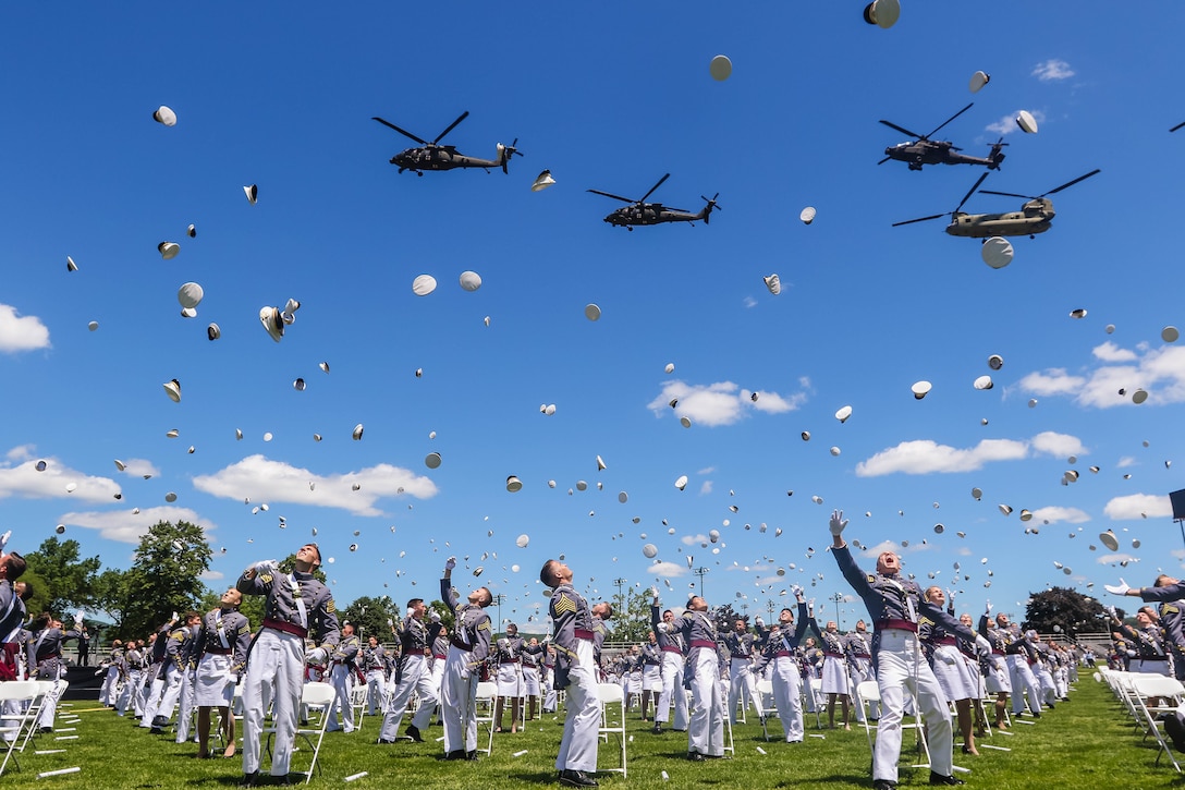 Cadets throw their hats in the air as a group of helicopters fly above them.