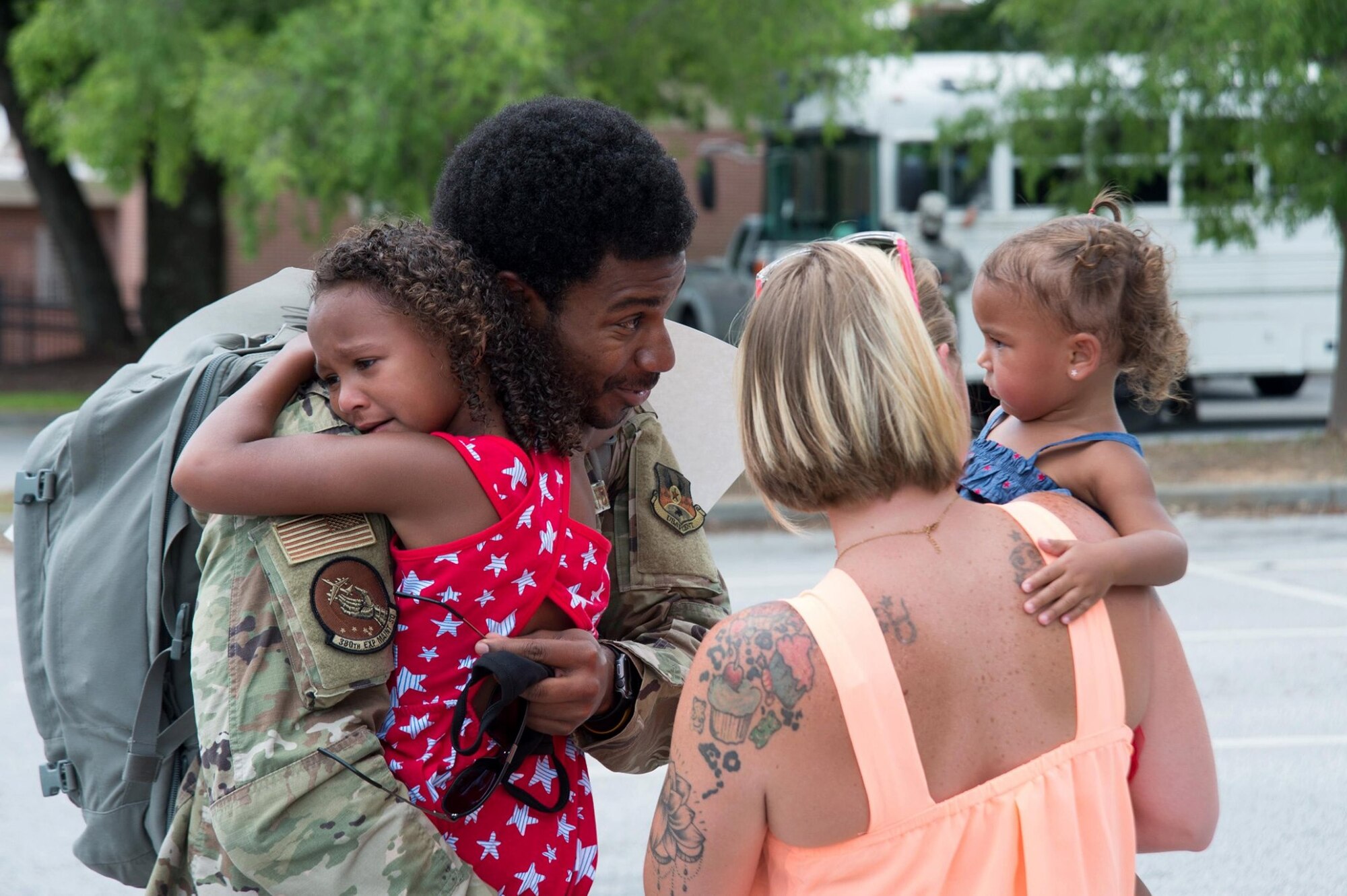 Photo of a service member hugs one of his daughters while looking at his younger daughter held in her mother's arms.