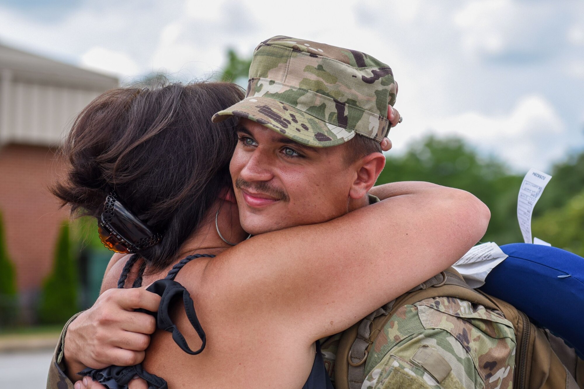 Photo of a service member smiling as a family member hugs him.