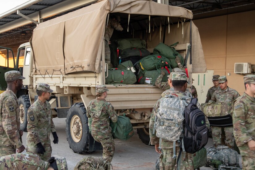 Soldiers pack gear into a military truck.