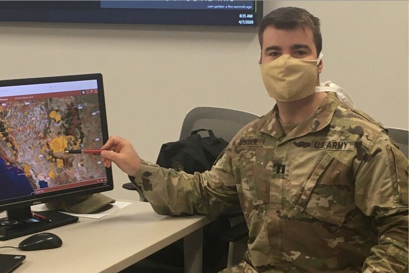 Soldier wearing a face mask points to an image on a computer monitor.