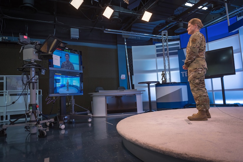 An airman standing in a television studio reads from a teleprompter.