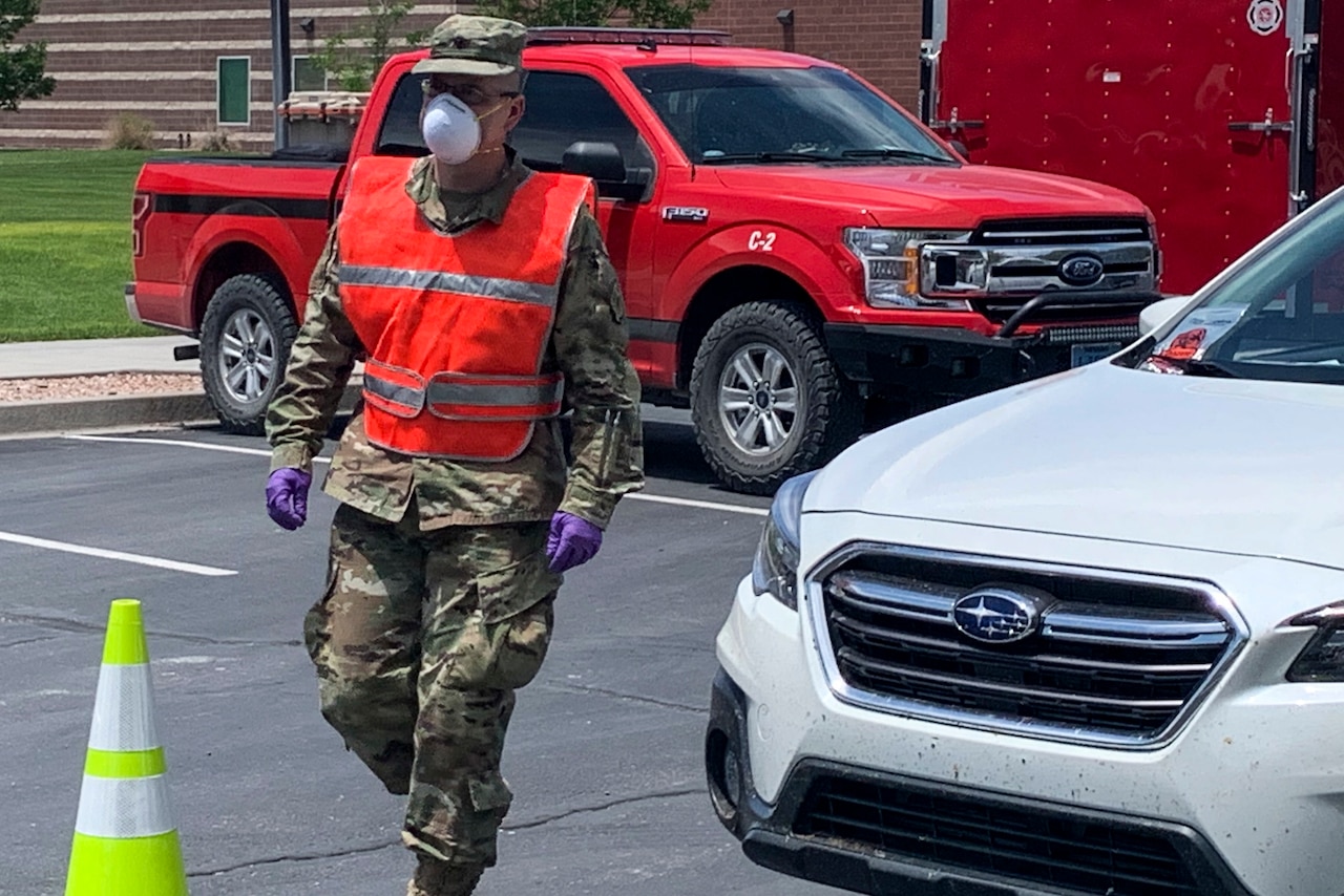 A soldier wearing a reflective vest and a face mask directs traffic.
