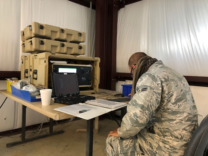 Photo shows an Airman reading a binder with equipment stacked on a table in front of him.