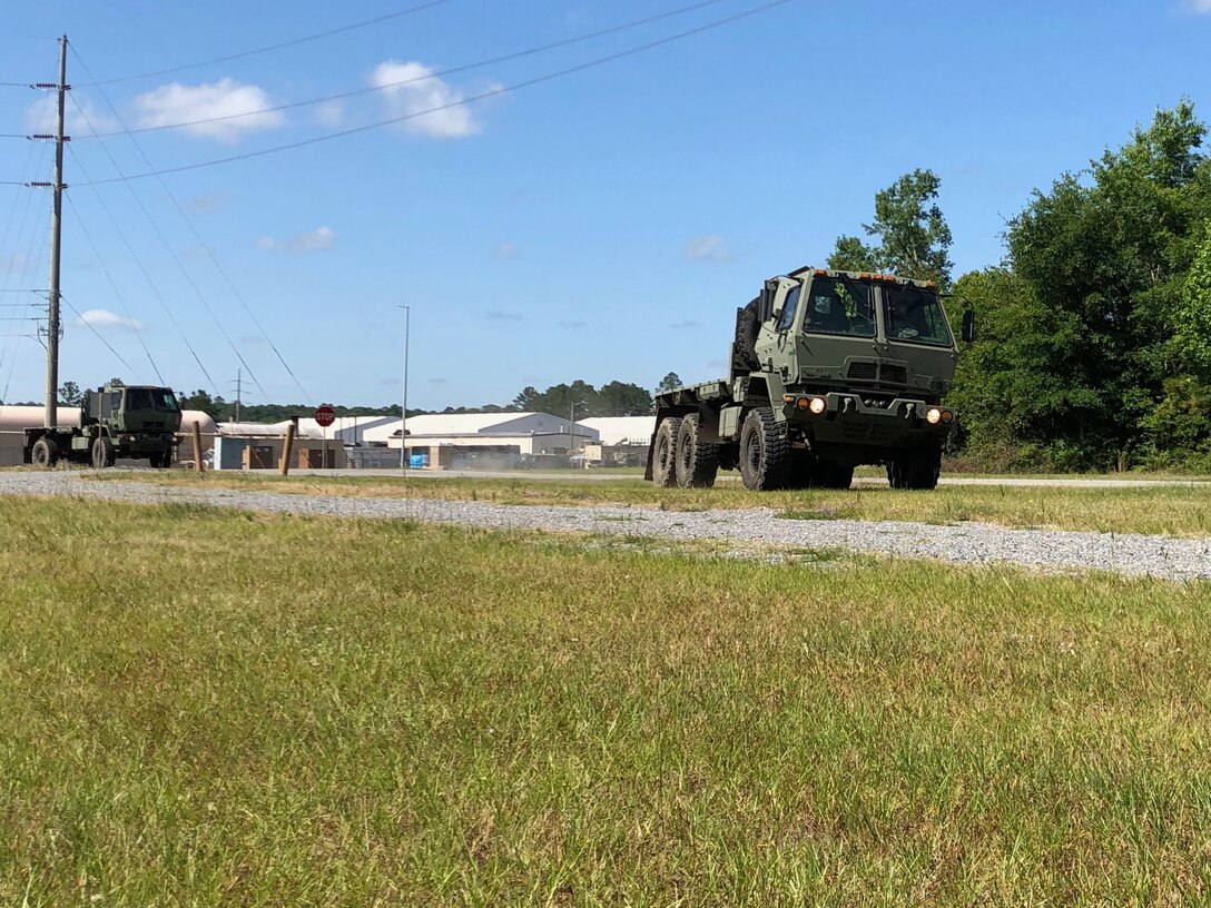 Photos shows large military trucks driving through grass next to a gravel road.