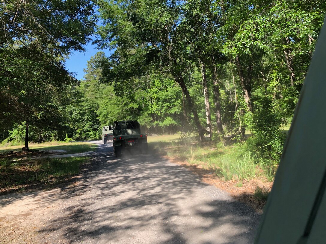 Photo shows large military truck driving down a small road lined with trees.