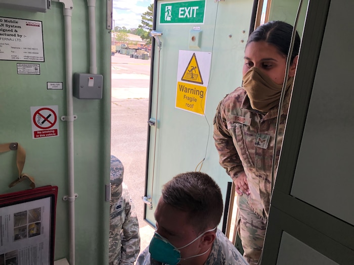 Photo shows an Airmen standing over the shoulder of another while he performs checks on equipment.
