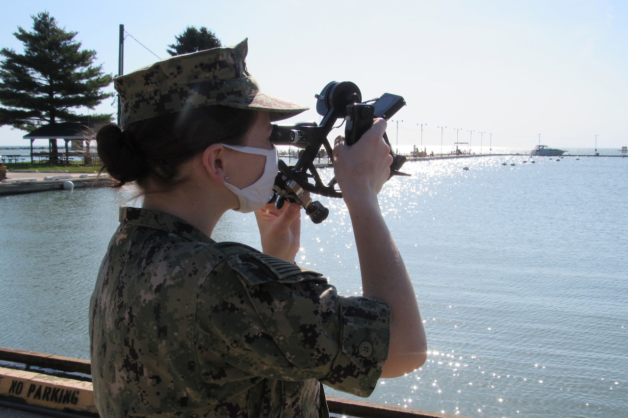 A sailor wearing a face mask trains in using a sextant.