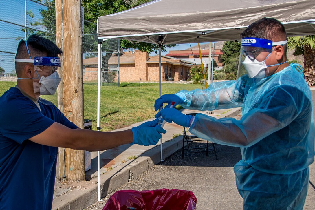 A guardsman wearing personal protective equipment is given a COVID-19 sample from another guardsman wearing personal protective equipment at a testing center.