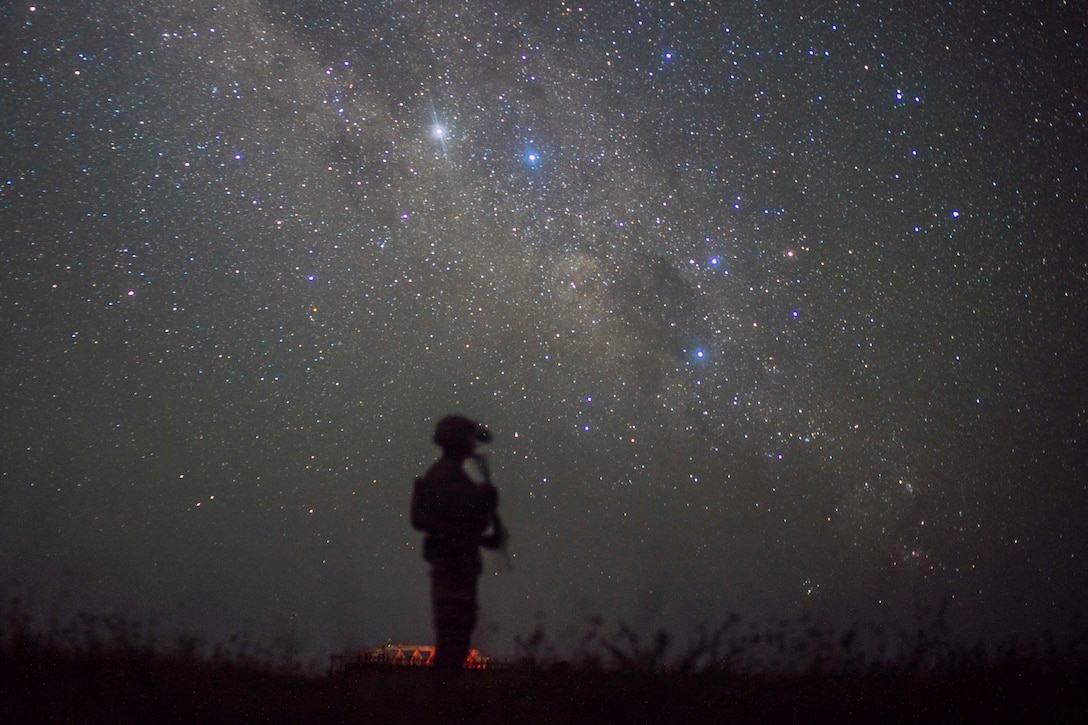 A soldier stands holding a weapon at night.