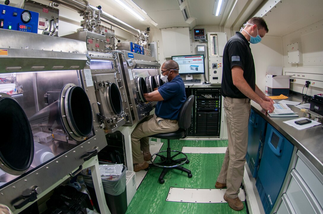 Two soldiers wearing masks work in a lab.