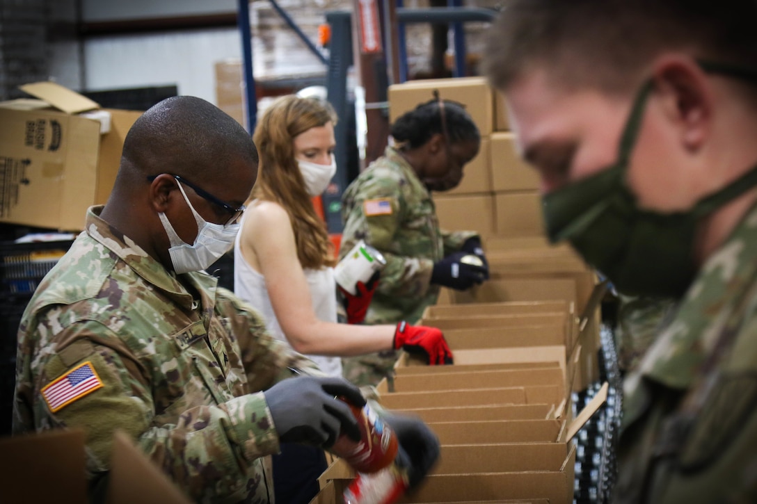 Soldiers and civilians work together to package food on an assembly line.