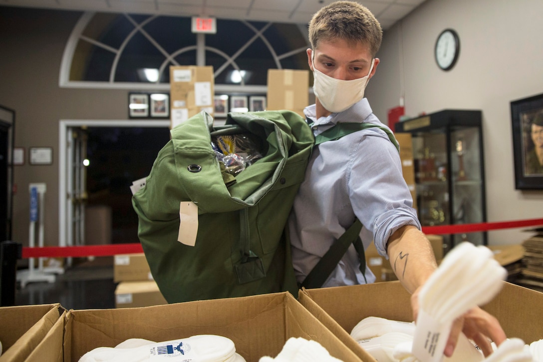 A Marine Corps recruit wearing a mask reaches into a bin of socks.