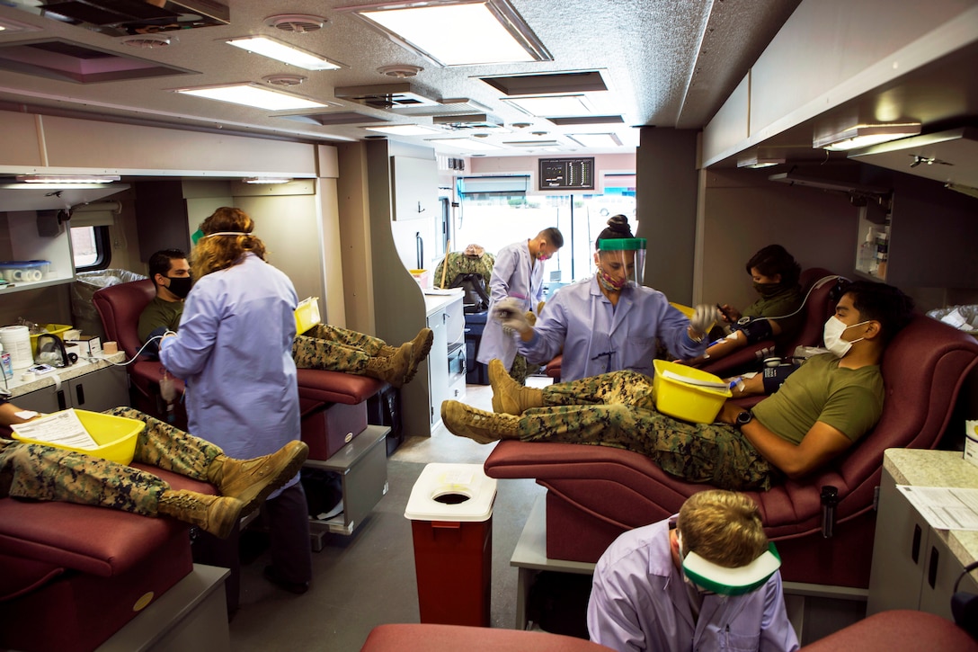 Inside a mobile blood drive facility, Marines and sailors wearing masks are tested by medical personnel wearing personal protective equipment.