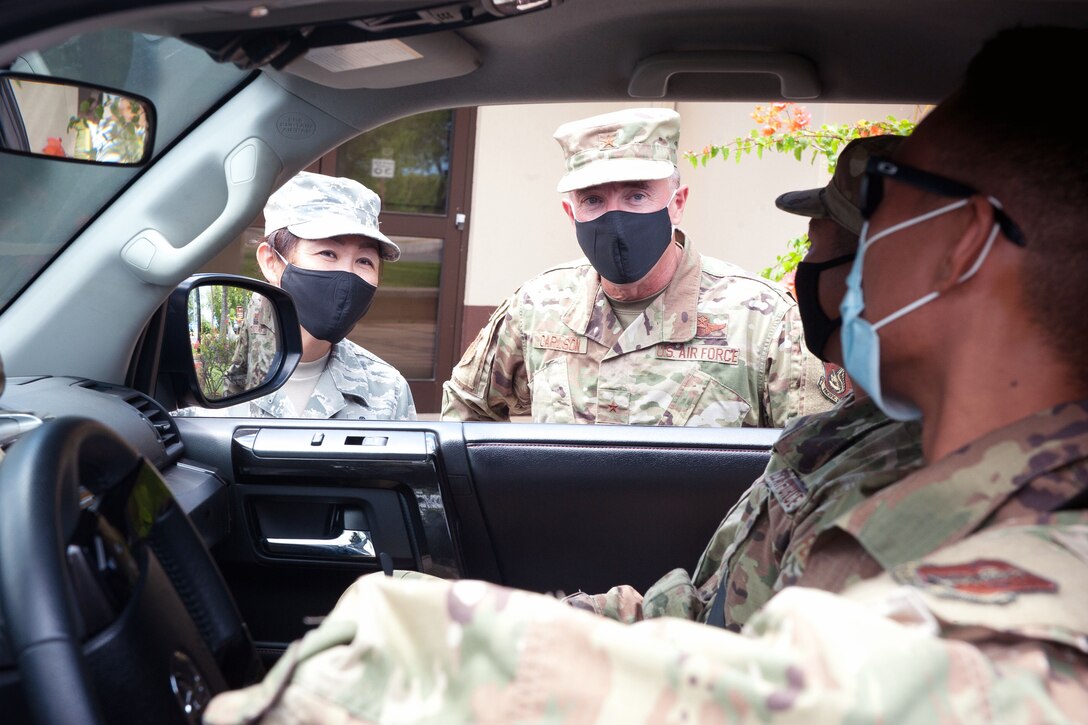 Two senior officers wearing masks speak to two airmen wearing masks at a take-away lunch station.