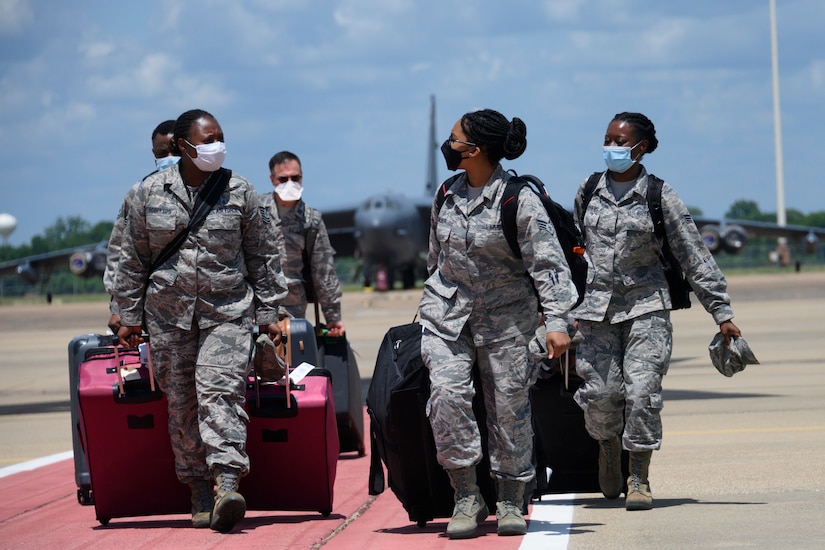 Airmen wearing face masks pull rolling suitcases while walking on a flight line.