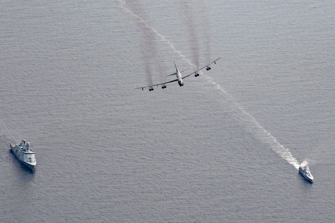 An aircraft flies over two ships.