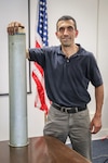 Senior interior ballistics engineer Ed Tersine stands with a Mark 9 cartridge case at Naval Surface Warfare Center Indian Head Explosive Ordnance Disposal Technology Division, June 11. Tersine’s expertise and insight in the field of Navy Gun Propulsion earned him the Dr. Delores M. Etter Award for Top Scientists and Engineers for 2019. (U.S. Navy photo by Matthew Poynor)