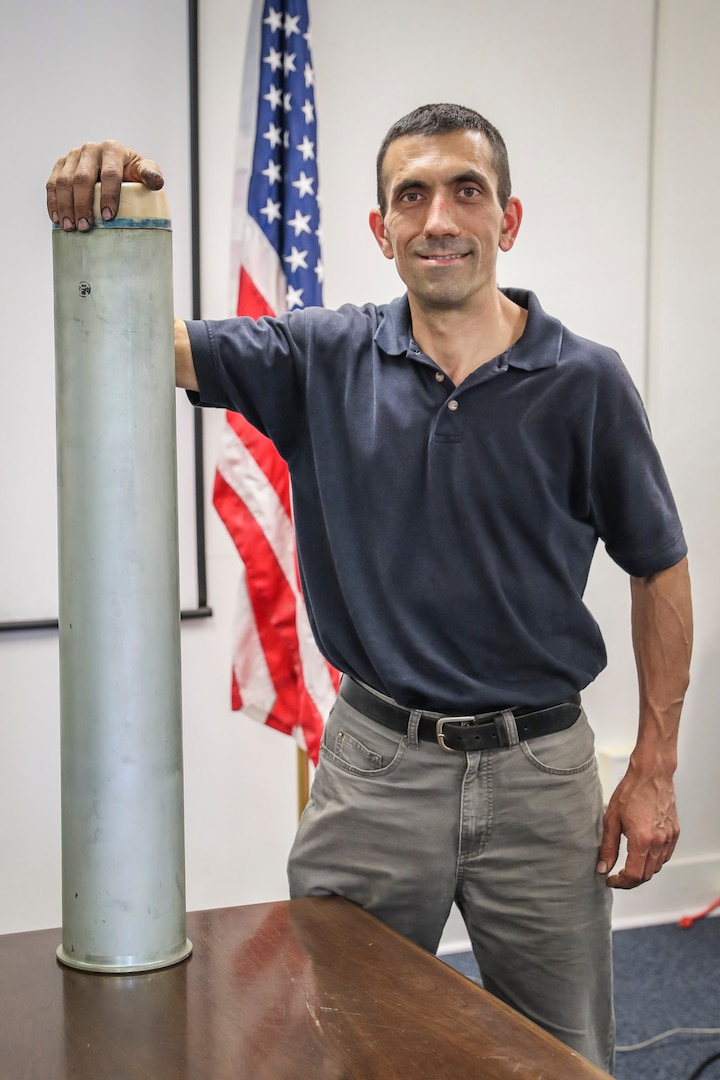 Senior interior ballistics engineer Ed Tersine stands with a Mark 9 cartridge case at Naval Surface Warfare Center Indian Head Explosive Ordnance Disposal Technology Division, June 11. Tersine’s expertise and insight in the field of Navy Gun Propulsion earned him the Dr. Delores M. Etter Award for Top Scientists and Engineers for 2019. (U.S. Navy photo by Matthew Poynor)