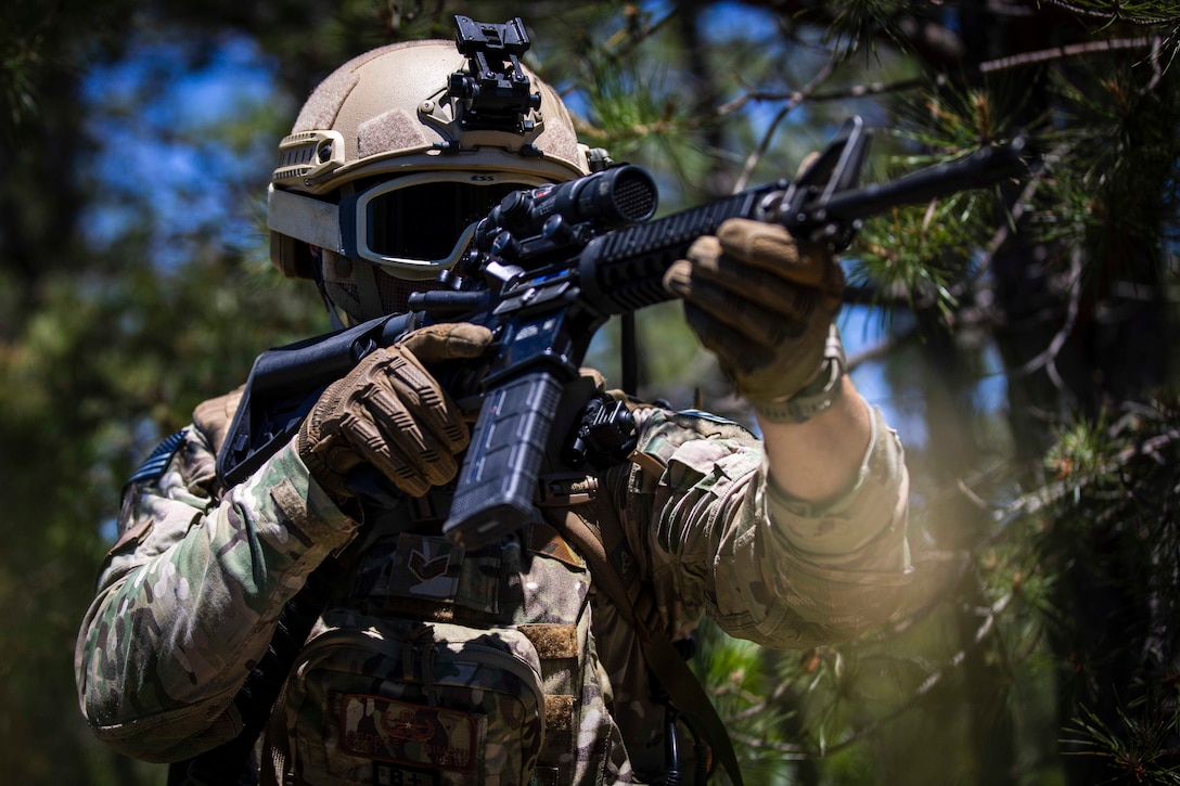 An airman wearing a helmet and goggles looks through the scope of a weapon.