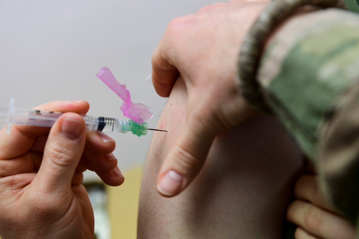 A service member pushed a hypodermic needle into a  person’s arm.