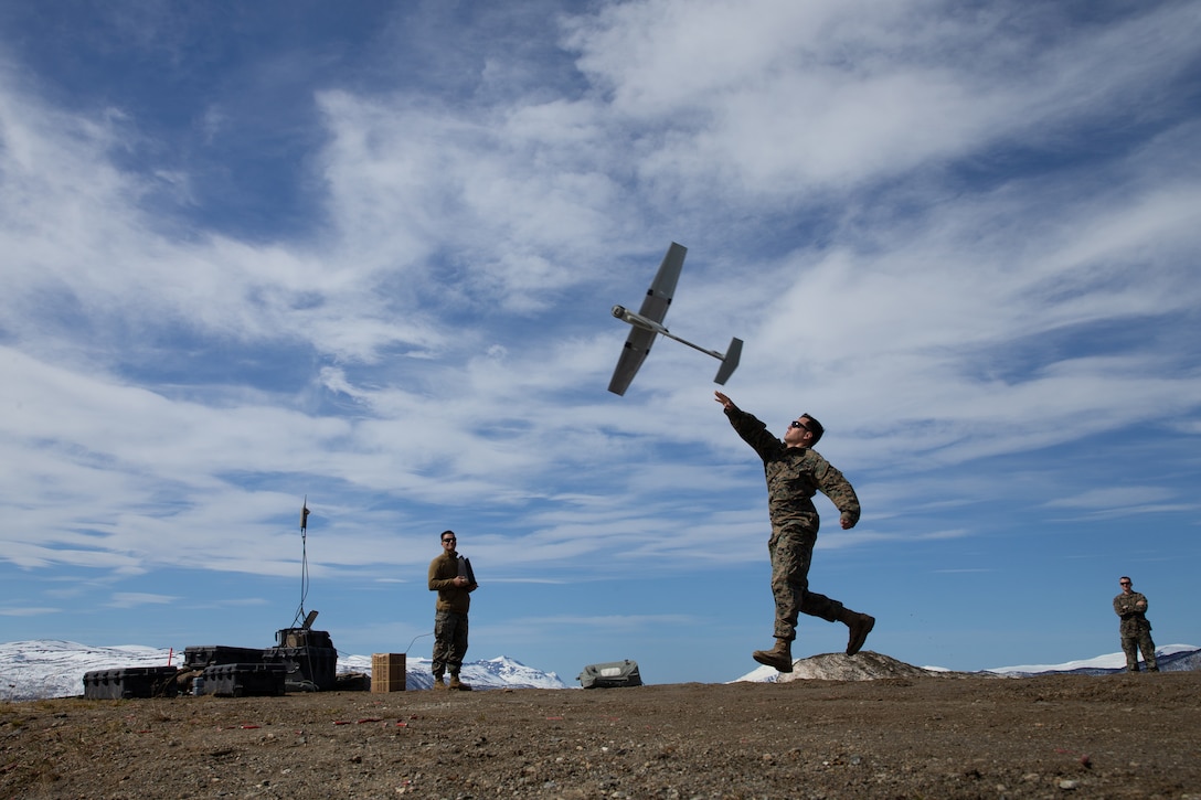 A service member launches a drone as two other service members watch from a distance.