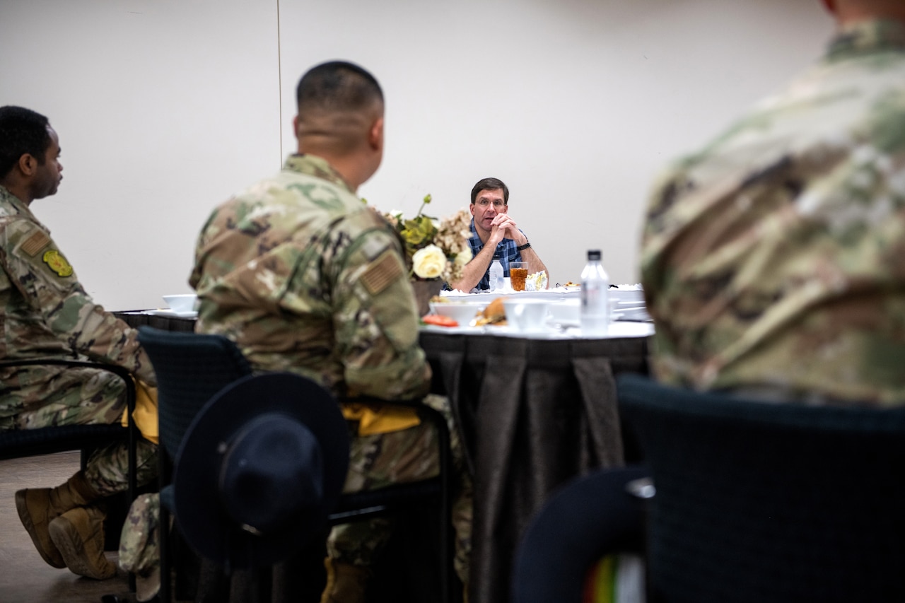 A civilian seated at a table talks with airmen during a working lunch.