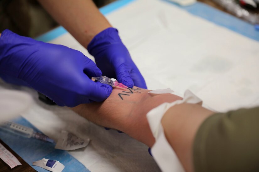 Gloved hands insert an IV catheter into an arm.