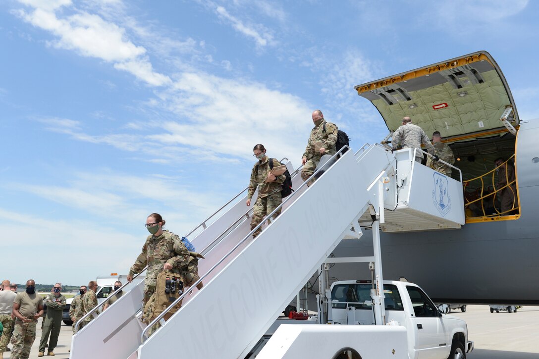 Airmen wearing masks descend the steps from an airplane.