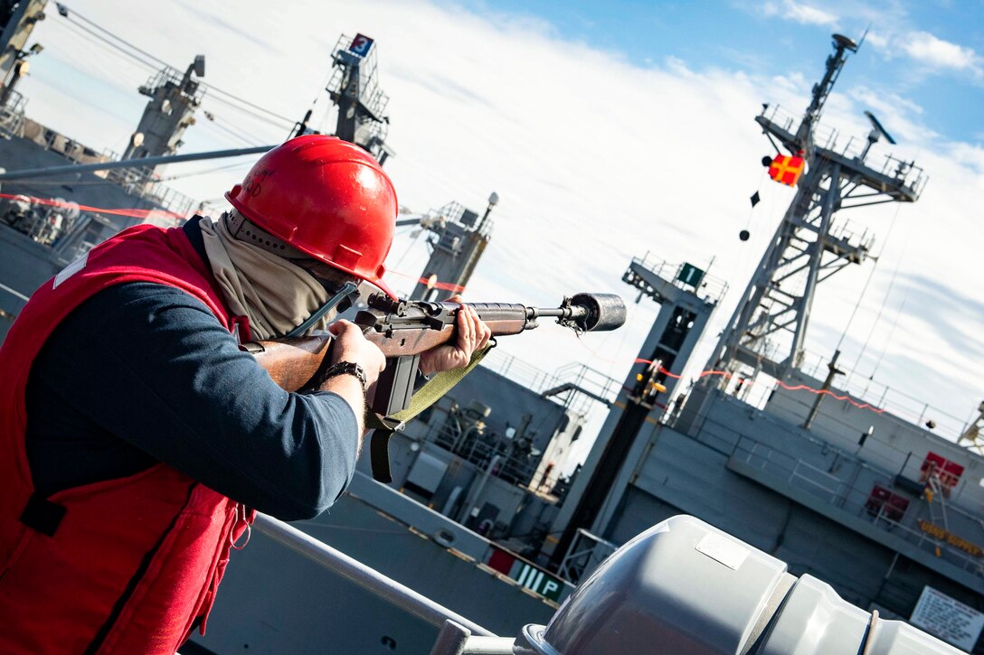 A sailor fires a line to another ship.
